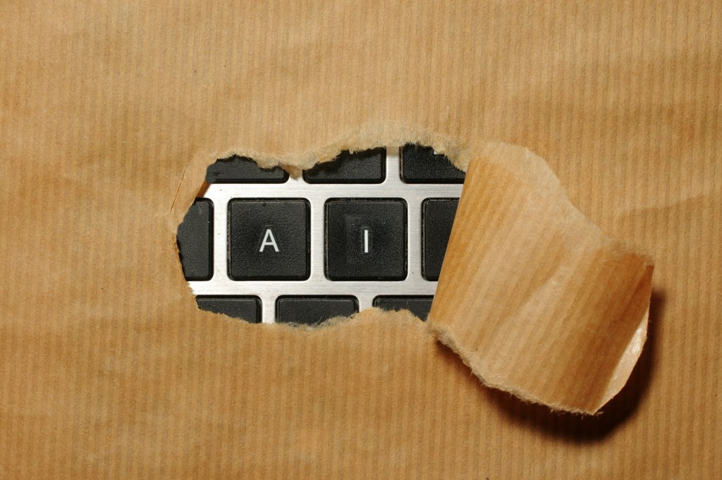 Brown piece of paper covers a computer keyboard. Through a ripped hole in the paper, the keys "A" and "I" are visible